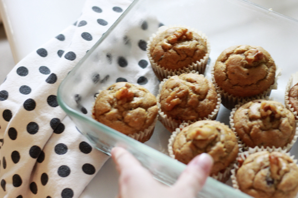 A rectangle glass dish full of peanut butter chocolate chip banana bread muffins sitting on a poka dot dishcloth with hand holding dish