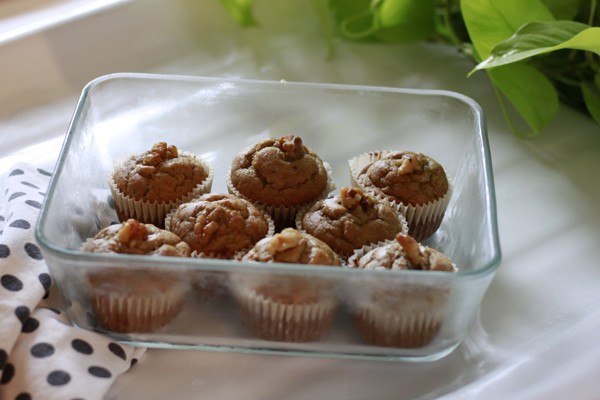 A rectangle glass dish full of peanut butter chocolate chip banana bread muffins sitting on a poka dot dishcloth with green leaves in background