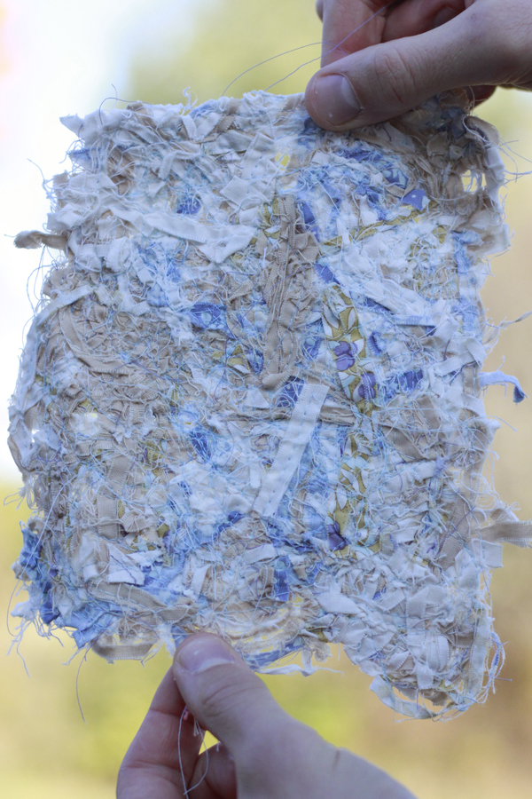 Blue, biege and white scrap fabric with blue thread held by two hands. 