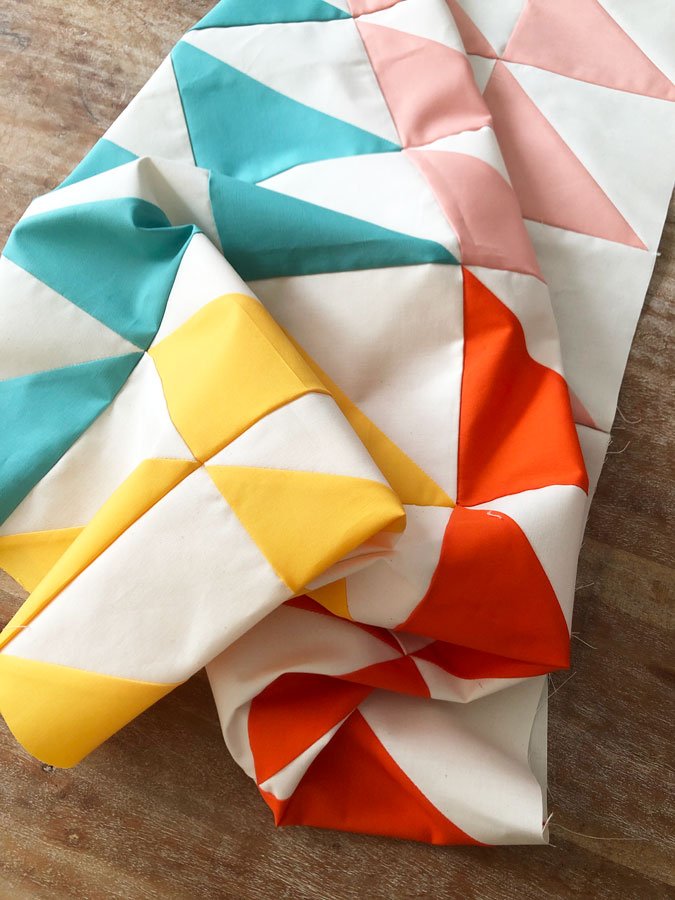 A quilt with raw edges, teal, yellow, peach and cream triangle design 