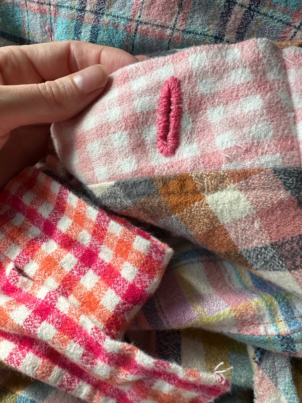 A pink button hole on pink gingham waistband of a fleece skirt. 