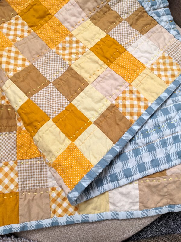 A winnie the pooh quilt theme, hand stitching in shades of a yellow. The back is blue and white gingham