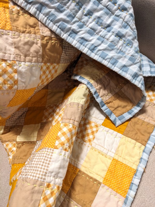 A winnie the pooh theme quilt, hand stitching in shades of a yellow. The back is blue and white gingham