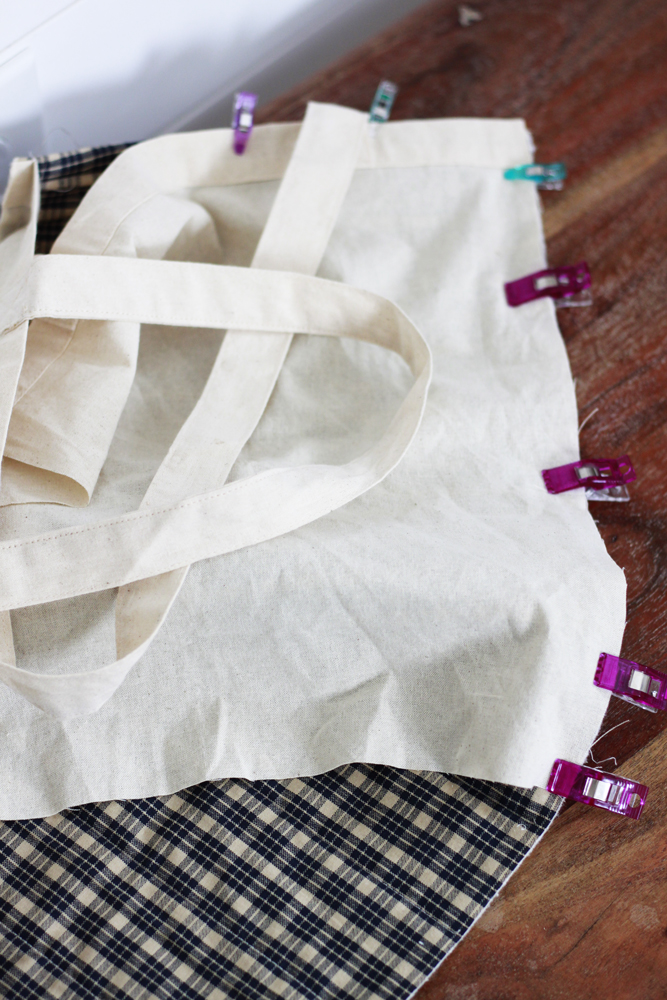 This canvas bag is clipped together with a panel of quilted fabric. There is shiplap in the background and the object sits on a wooden table.