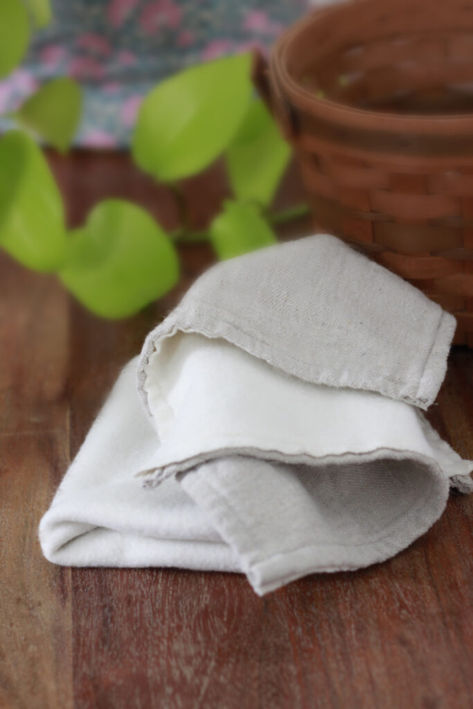 A thick cloth with fleece on one side and grey textured on the otherside. it lays on a dark wood table with a plant, basket in the background