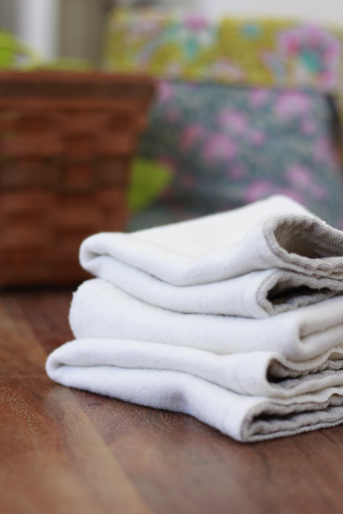 fleece linens folded with textured grey on the other side are on a dark wood table. baskets are in the background one is floral the other is wicker