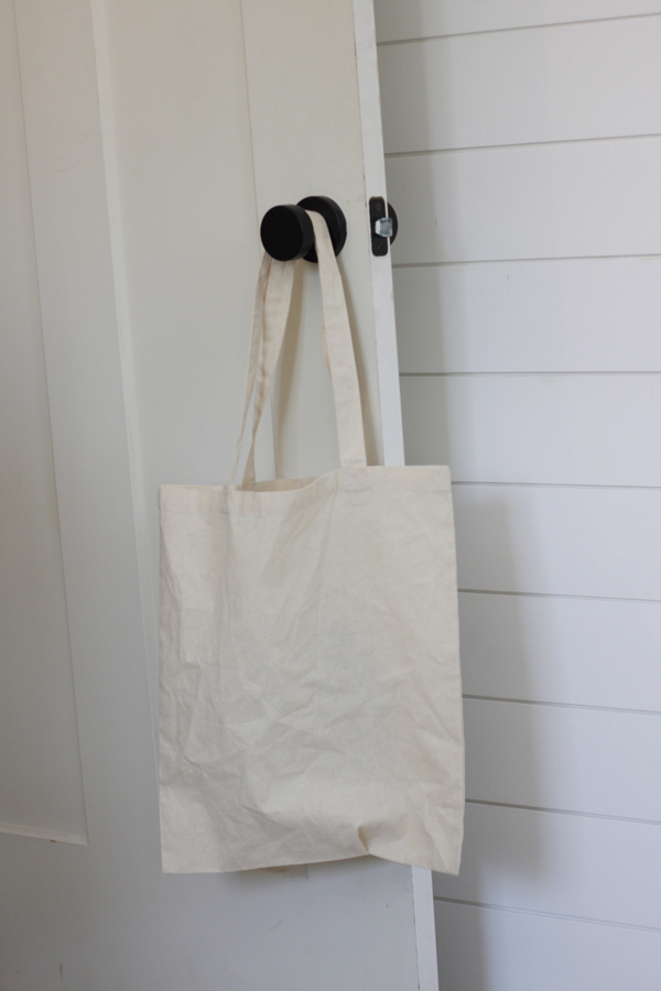 A plain canvas bag hanging on a black door knob with white ship lap in the background