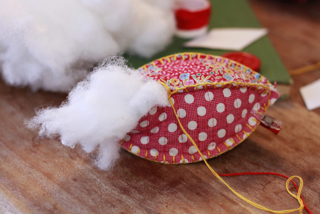 craft ornament with christmas fabrics, poka dot and floral with stuffing coming out of it. 