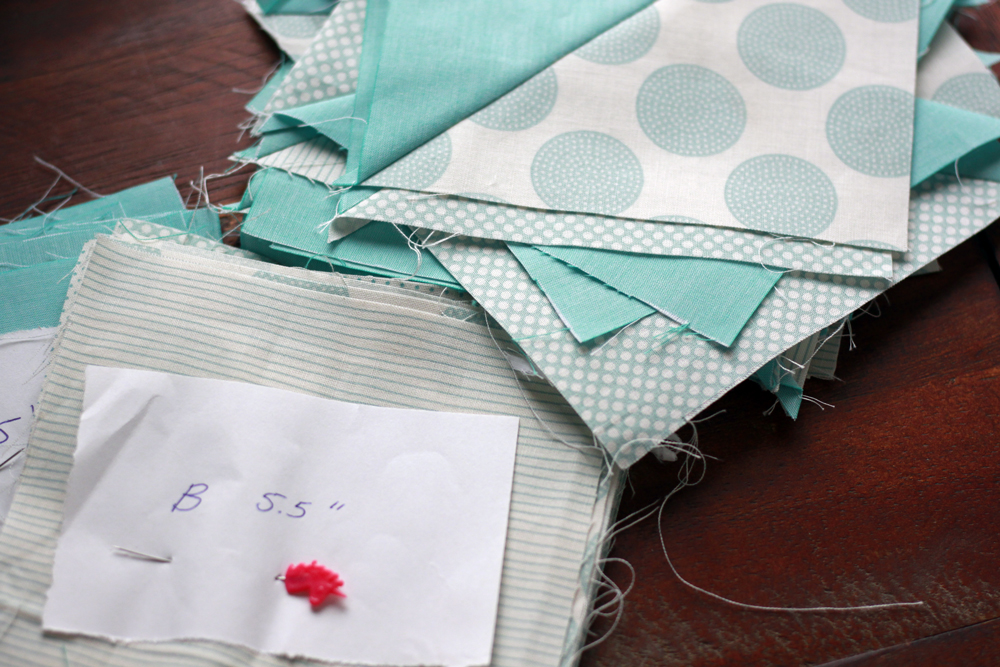multiple piles of fabric pieces cut into squares. there is a label on the pile that says "B 5.5" 